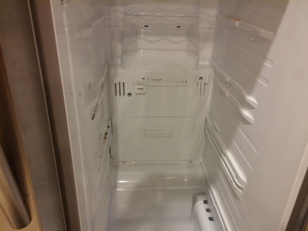Freezer compartment with metal racks taken out. Panel to expose defrost system in back of fridge.